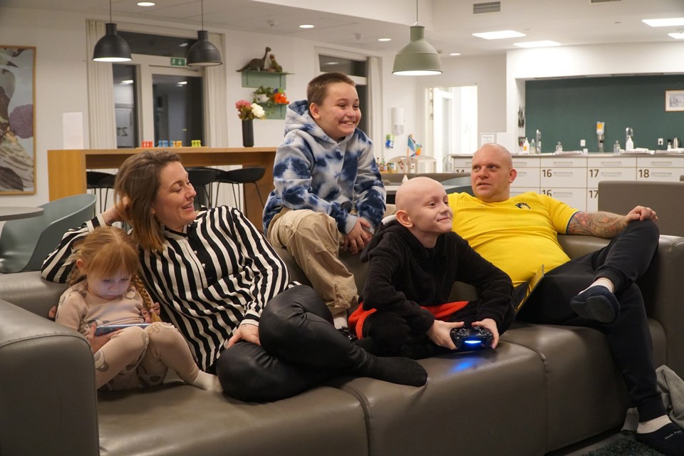 Familie med tre barn sitter i en sofa. To av dem spiller på konsoller. 