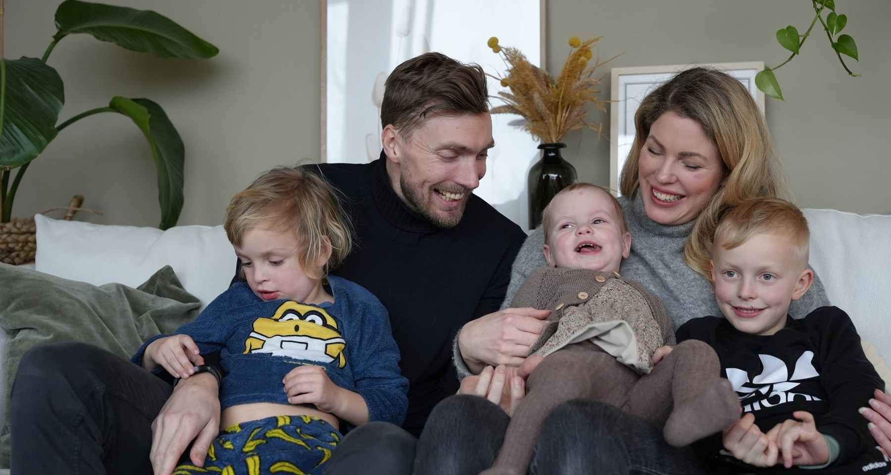 En familie på fem smiler og ler i en sofa.